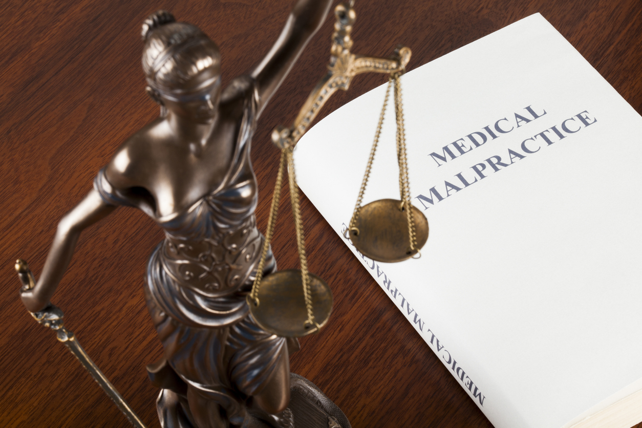 A statue of Lady Justice and a law book about medical malpractice.